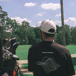 Person wearing a black t-shirt with a graphic design, standing on a golf course.