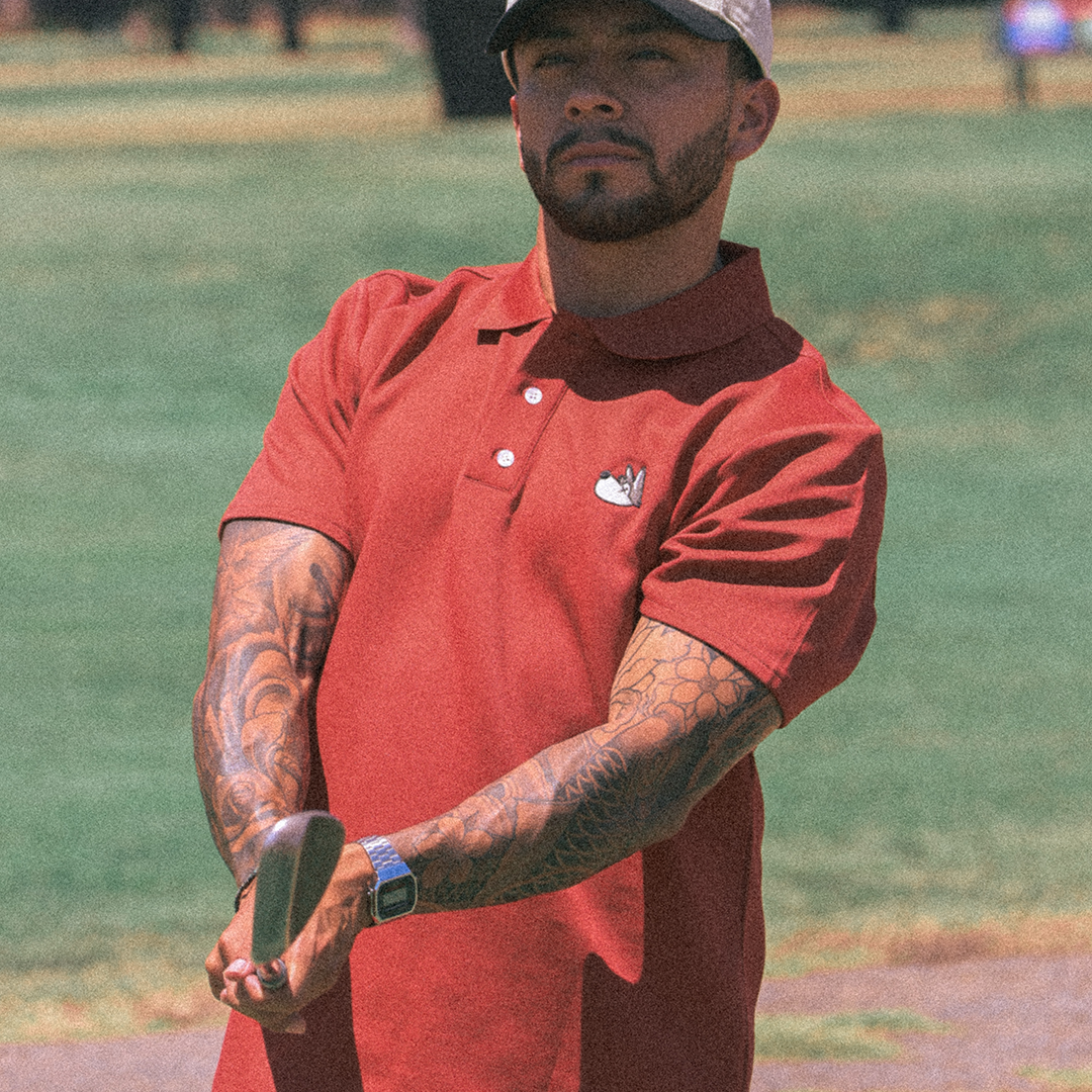 Man in a red polo shirt and cap holding a club on a golf course
