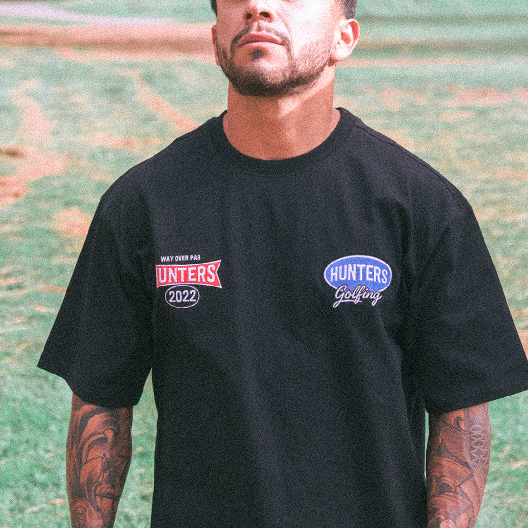 Man wearing a black t-shirt with 'Hunters' logos outdoors