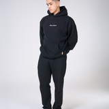 Person wearing a black hoodie and pants with a logo on a white background