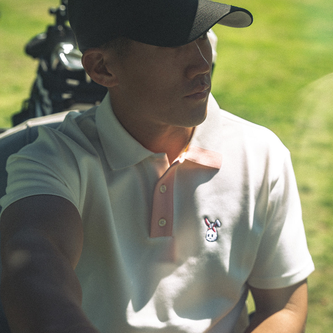 Man in a white polo shirt with a logo, sitting on a golf course.