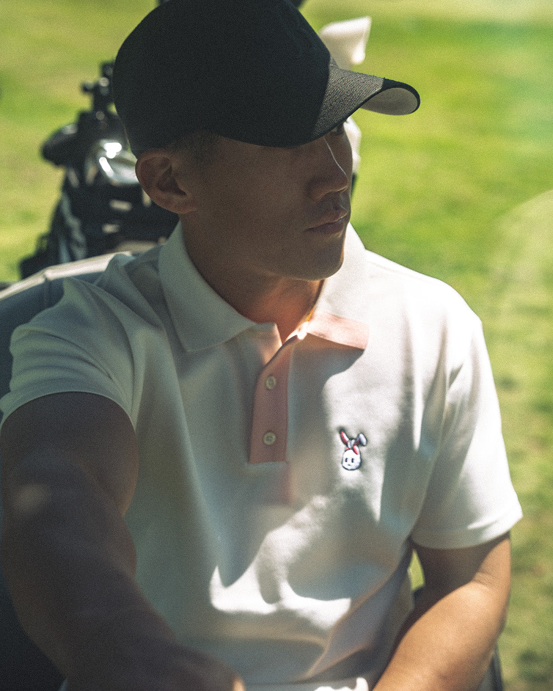 Man in a white polo shirt with a logo, sitting on a golf course.