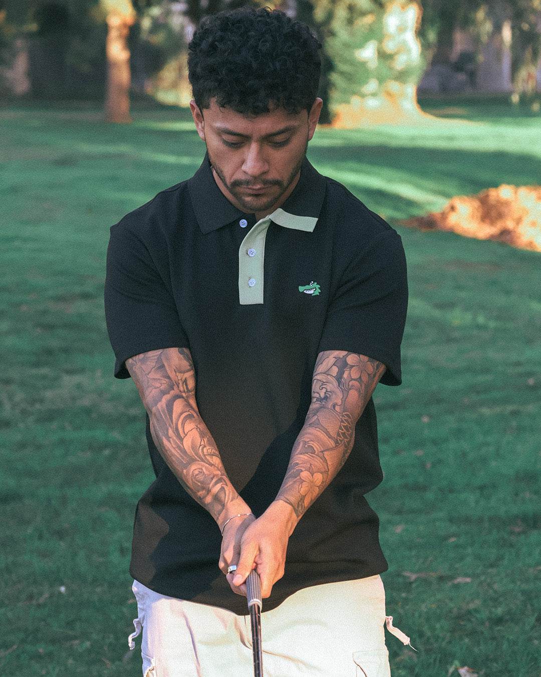 Man in black polo shirt with green logo holding a golf club on a golf course