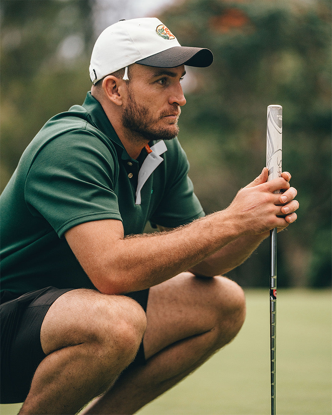 Man in green shirt and white cap holding a golf club on a golf course