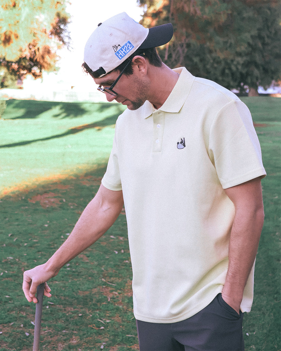 Man on a golf course wearing a white cap and beige polo shirt.
