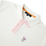 A cream polo shirt with a white and pink embroidered bunkie emblem on the chest, pink contrast on the button placket and collar, and a relaxed fit.
