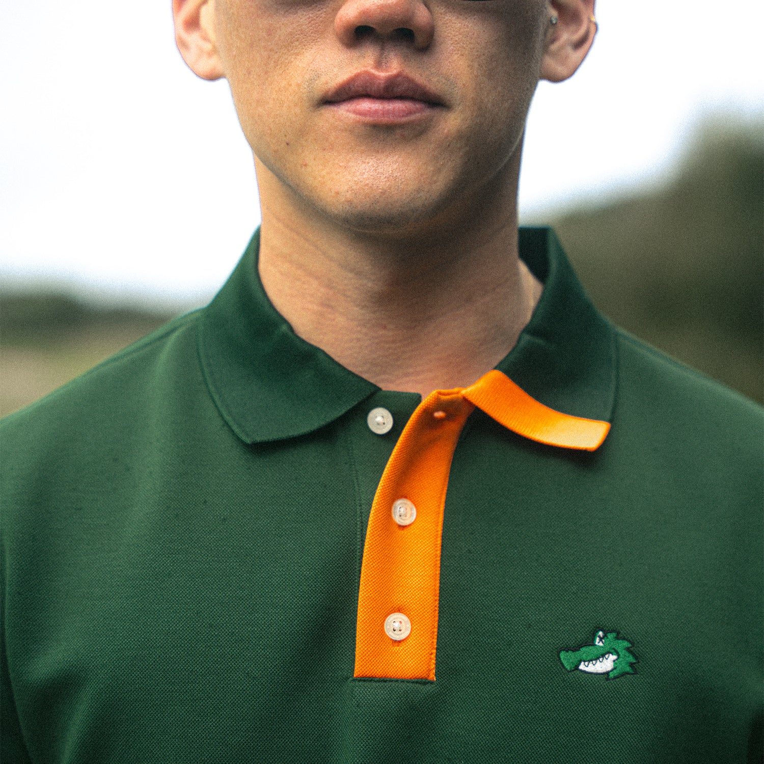 Close up of man wearing green polo shirt with crocodile embroidery and orange collar accent.