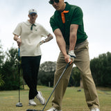 Two man standing holding golf clubs. One is wearing a green polo with orange accents the other is wearing a white polo with green accents.