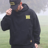 Person wearing a black hoodie with a yellow logo and text, standing outdoors in foggy weather.